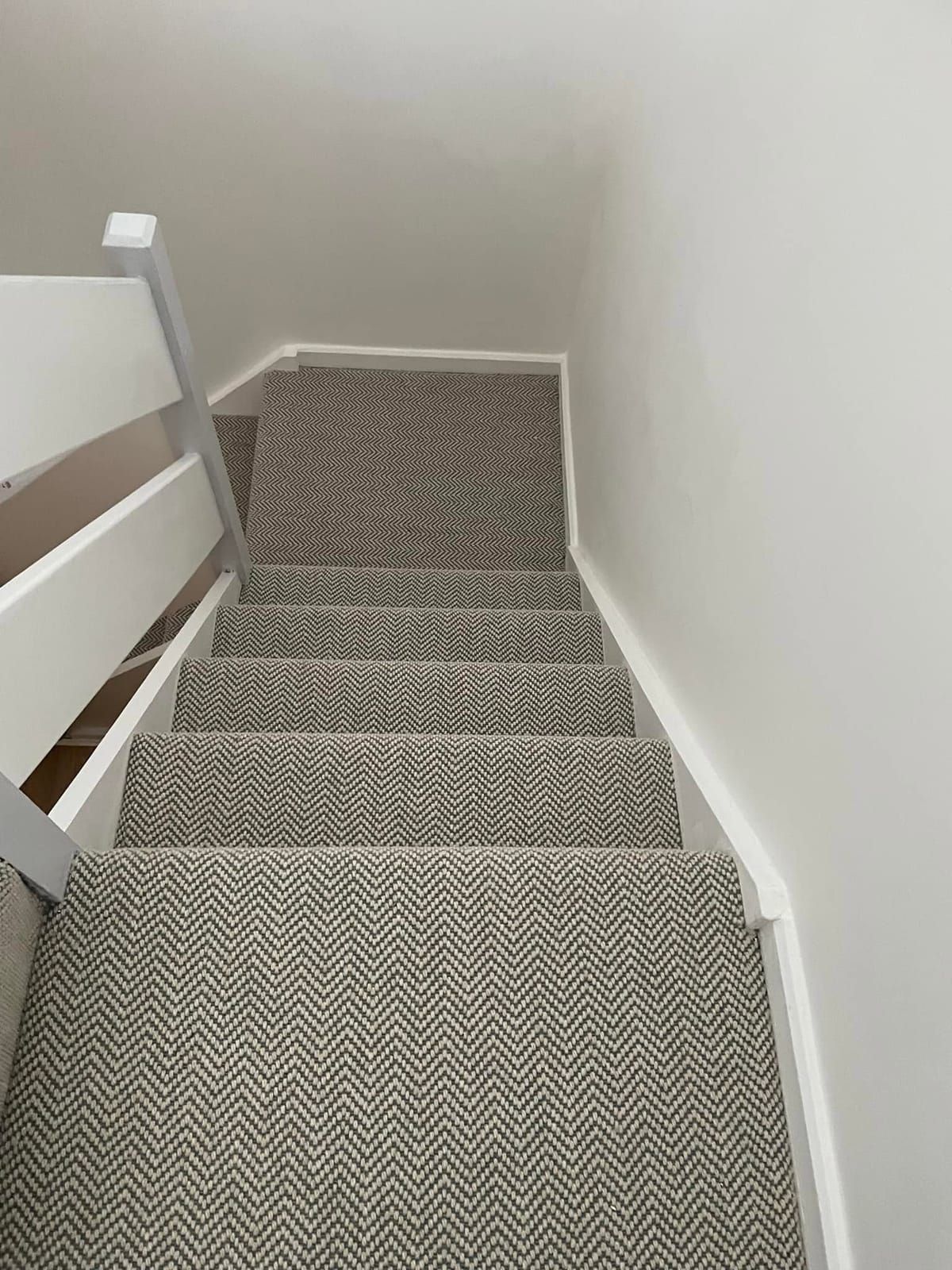 Looking down a staircase carpeted in grey herringbone