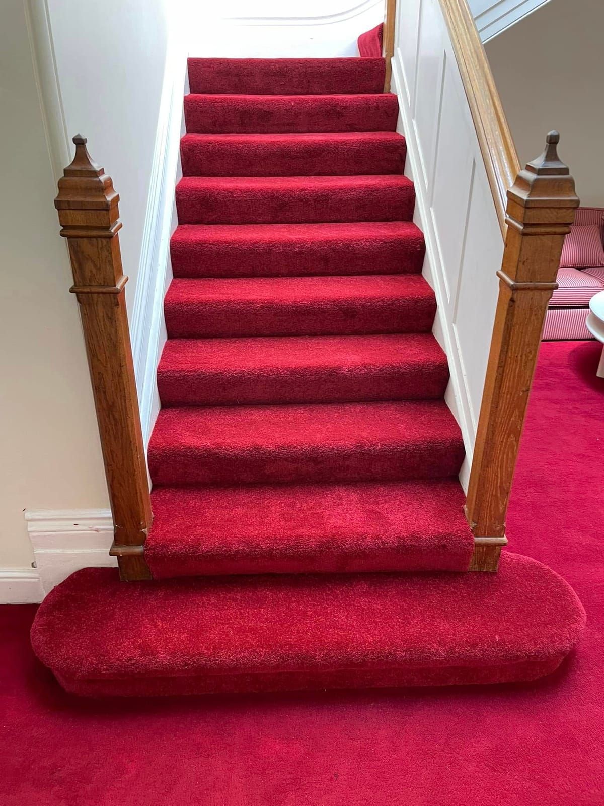 Red carpet on a straight staircase with oak newel posts and a bullnose bottom step