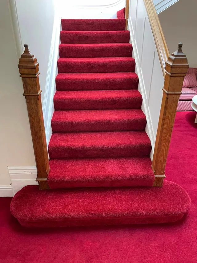 Red carpet on a straight staircase with oak newel posts and a bullnose bottom step