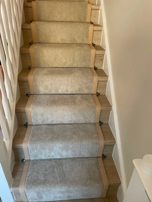 Grey stair runner with bound edges and antique brass stair rods on oak-effect treads